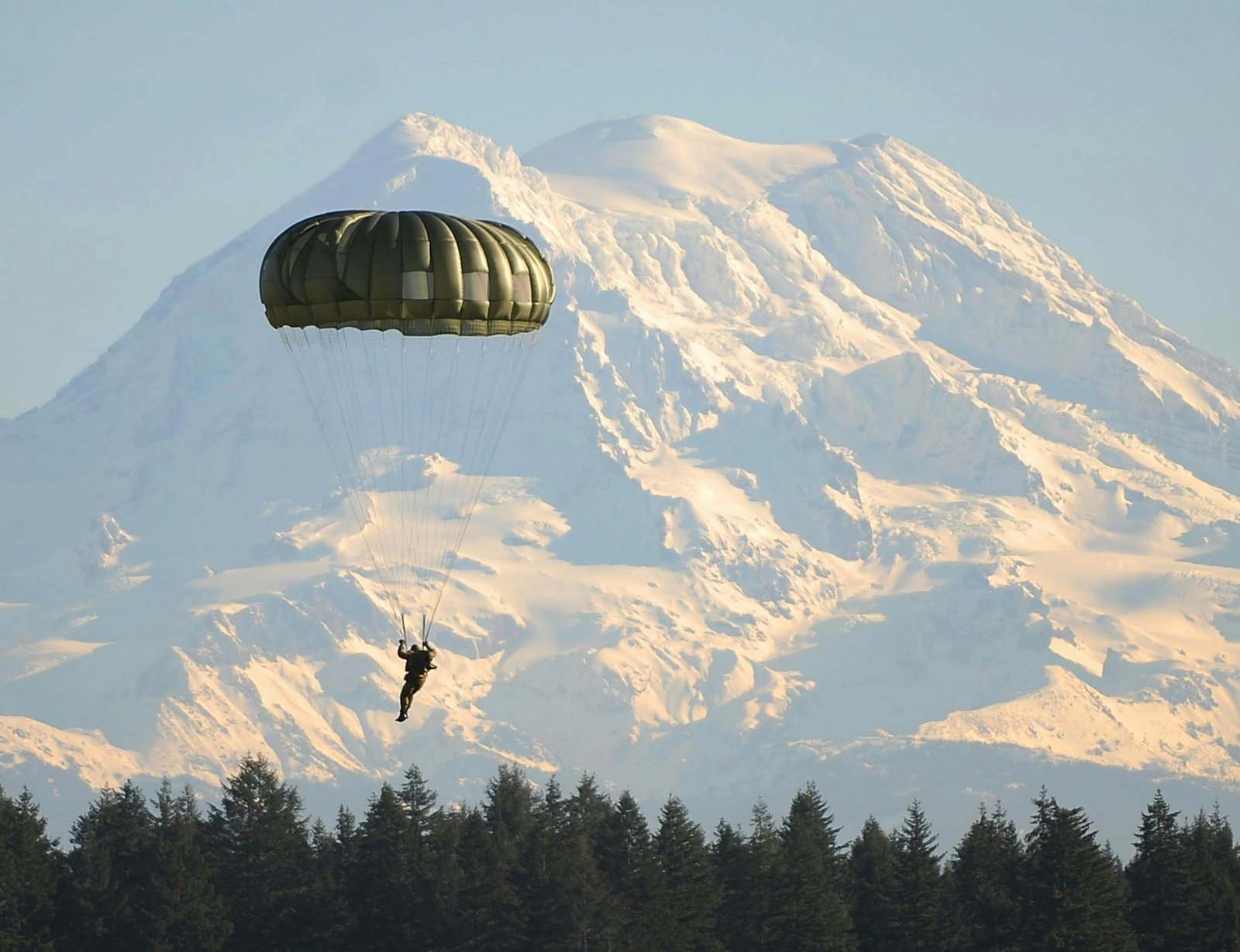 A parachutist descends gracefully with a snow-covered mountain in the background, surrounded by winter wilderness.