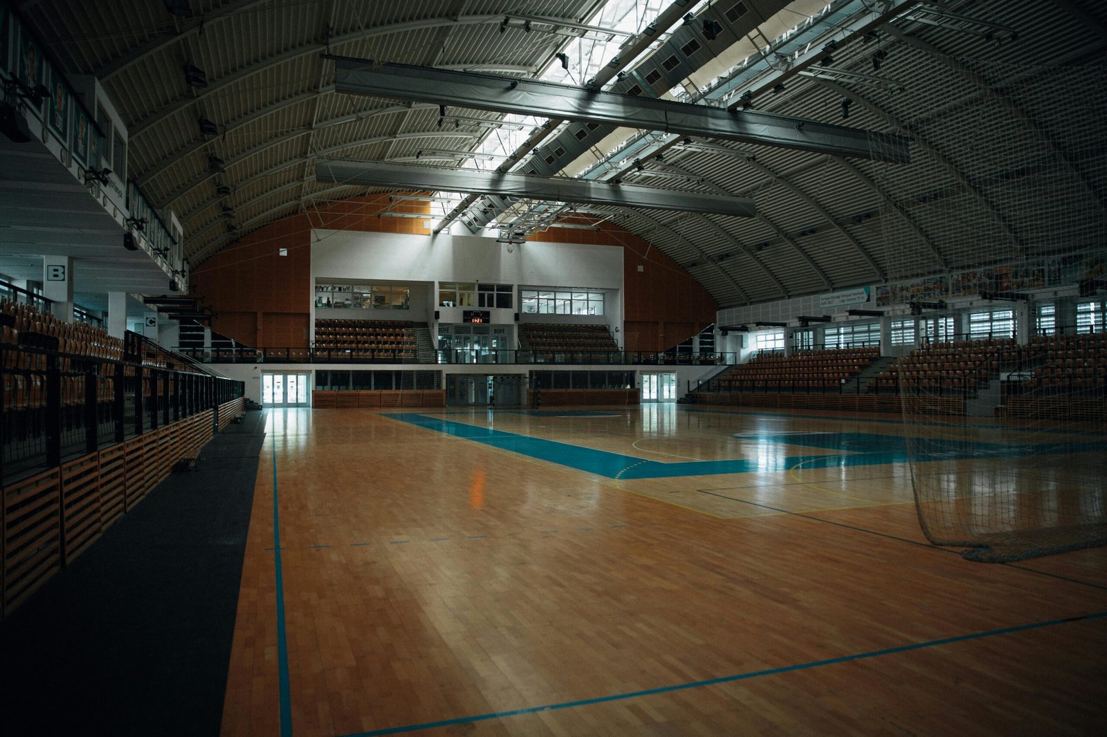 Empty indoor sports arena with hardwood flooring and bleachers, perfect for various sports activities.